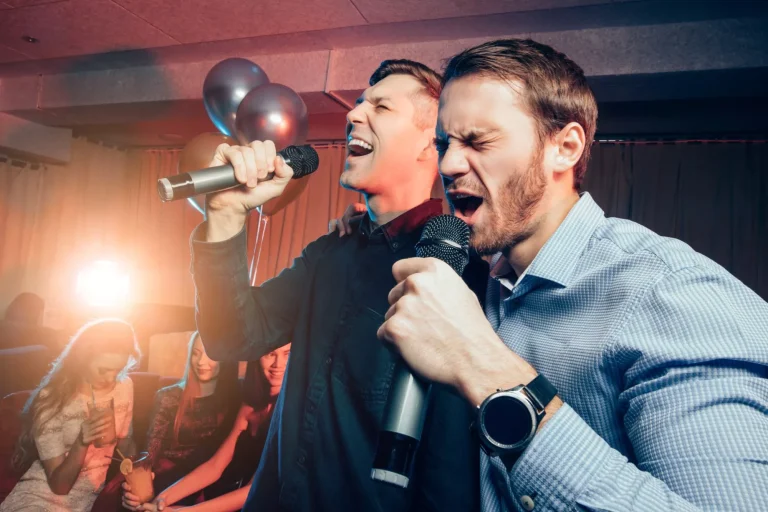 zwei junge kaukasische Männer in T-Shirts singen am Mikrofon in einer Karaoke-Bar, haben Spaß, feiern. Urlaub, Freizeit, Party Konzept