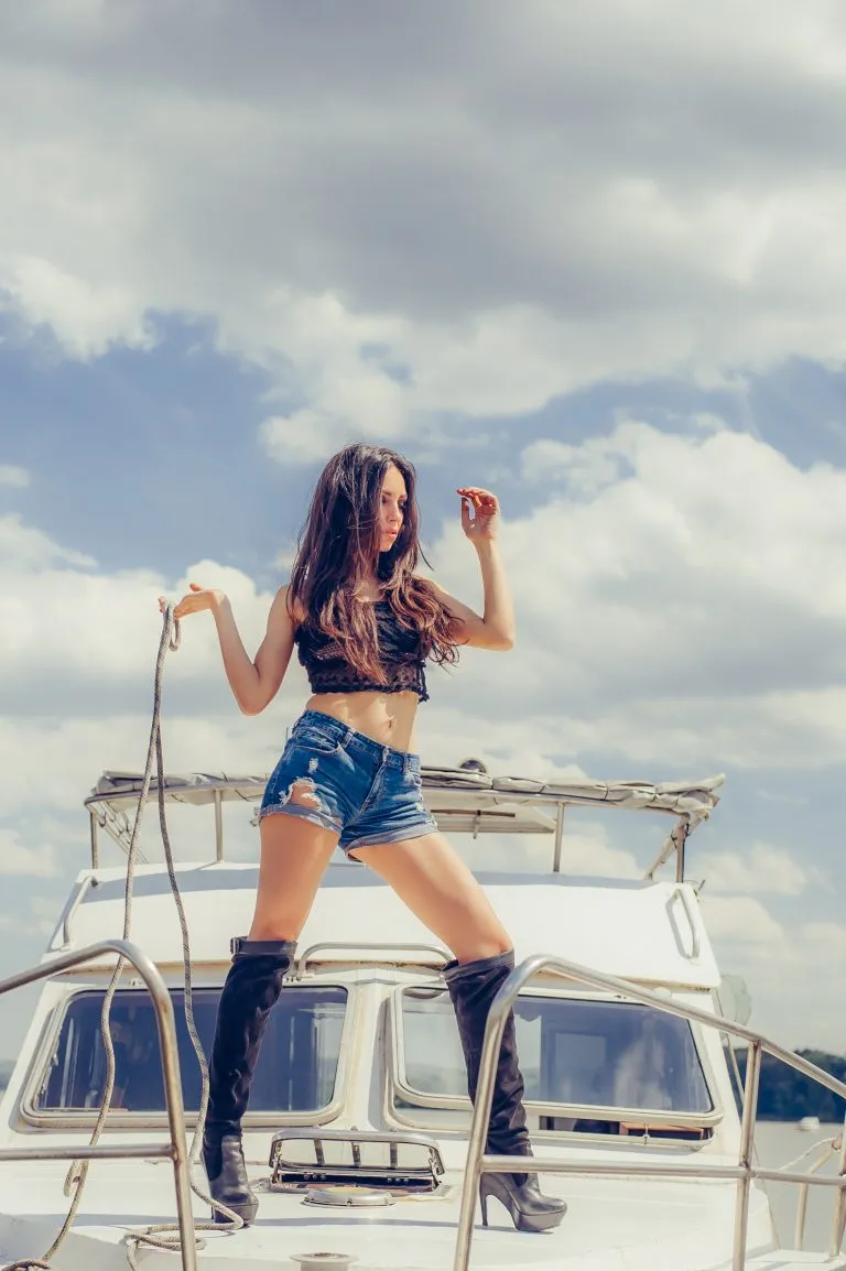 Heiße verführerische Frau in sexy hohen schwarzen Stiefeln posiert auf Boot